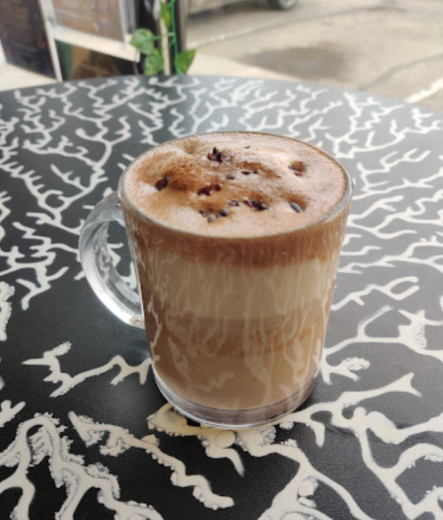 A clear glass mug filled with layered iced coffee on a patterned black and white table.