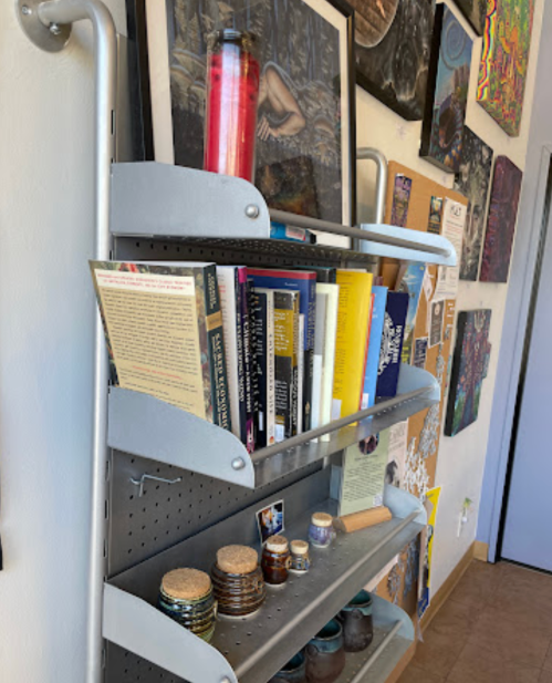 A metal bookshelf with books, jars, and art pieces displayed on the wall in a bright room.