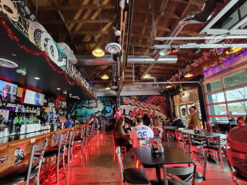 A lively bar interior with colorful murals, a long bar, and patrons enjoying drinks in a vibrant atmosphere.