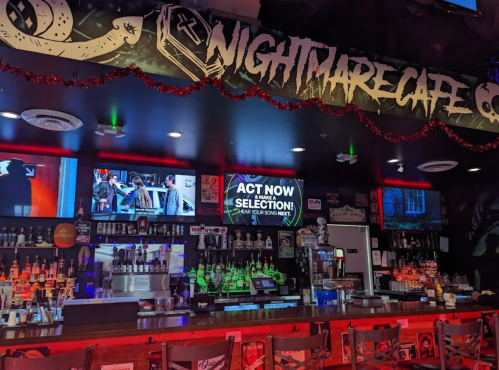 Interior of Nightmare Cafe featuring a bar, colorful lights, and screens displaying content. Festive decorations are visible.