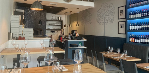 A modern restaurant interior with wooden tables, wine bottles on display, and a cozy atmosphere.