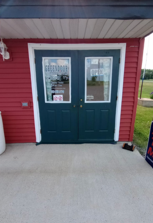 Exterior view of a red building with green double doors, featuring an "Open" sign and various business notices.