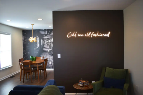 A cozy living space featuring a dark wall with a neon sign, a dining area, and modern furniture.