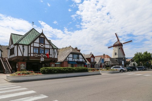 Charming village scene featuring Tudor-style buildings and a windmill under a partly cloudy sky.