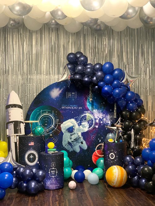 A colorful space-themed party setup with balloons, a rocket, and an astronaut backdrop.
