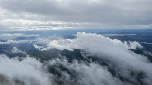 Aerial view of a cloudy landscape with rolling hills and distant lakes under a gray sky.