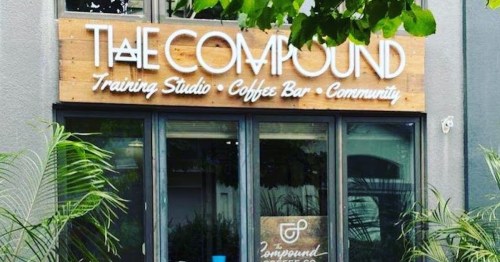 Exterior of "The Compound" featuring a training studio, coffee bar, and community space with greenery in front.