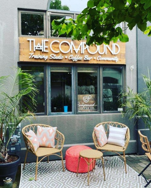 Exterior of "The Compound" featuring a coffee bar and training studio, with outdoor seating and greenery.