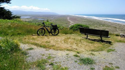 A bicycle parked beside a bench overlooking a scenic coastal landscape with fields and ocean in the distance.