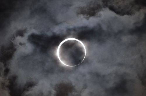A solar eclipse with a bright ring of light surrounded by dark, cloudy skies.