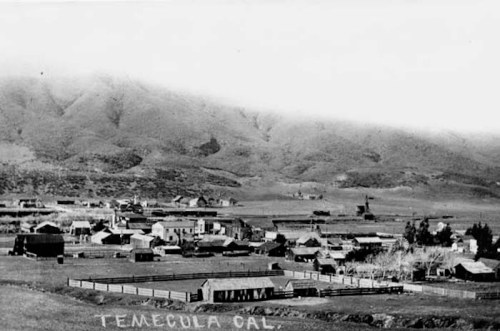 Black and white photo of early Temecula, California, featuring buildings and mountains in the background.