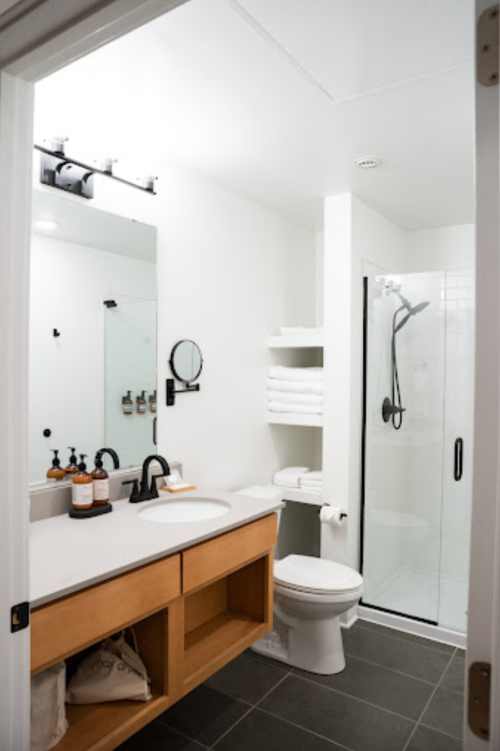 Modern bathroom featuring a shower, toilet, sink with wooden vanity, and neatly arranged towels. Bright and minimalist design.
