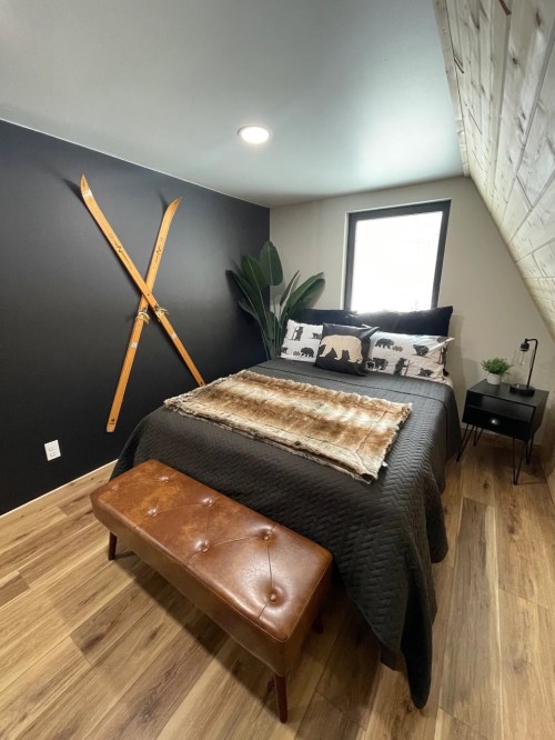Cozy bedroom with a black accent wall, wooden skis, a plant, and a bed adorned with decorative pillows and a fur throw.