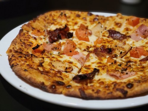 A close-up of a delicious pizza topped with cheese, tomatoes, onions, and various meats on a golden crust.