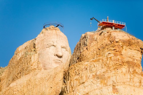 A large stone sculpture of a face on a mountain, with construction equipment nearby against a clear blue sky.