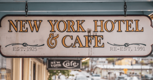 Sign for "New York Hotel & Café," established 1925, re-established 1991, hanging above a street.