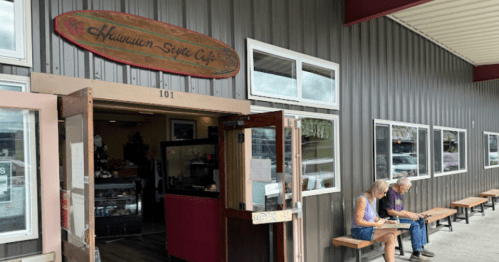 A Hawaiian-style café entrance with two people sitting outside on benches, enjoying their time.