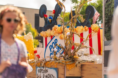 A colorful popcorn-themed float with decorations, featuring popcorn and corn stalks, at a festive outdoor event.