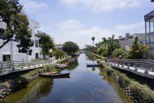 A serene canal lined with greenery and colorful houses, featuring small boats on the water under a clear blue sky.