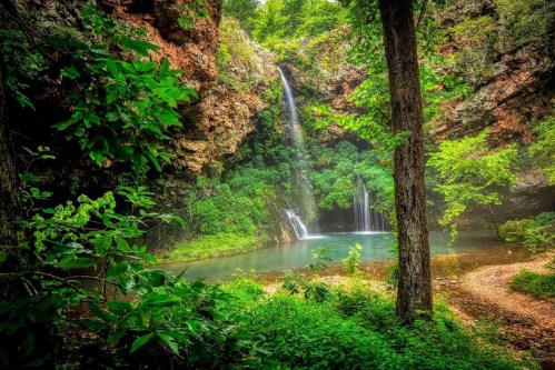A serene waterfall cascades into a tranquil pool, surrounded by lush greenery and rocky cliffs.