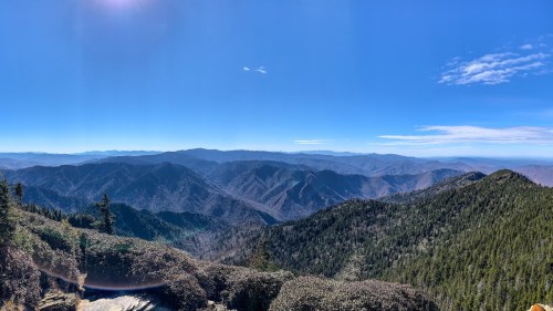 A panoramic view of rolling mountains under a clear blue sky, with lush greenery in the foreground.