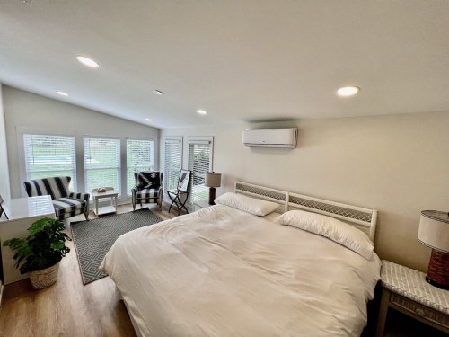 Bright bedroom with a large bed, two chairs, and natural light from windows, featuring a cozy, modern design.