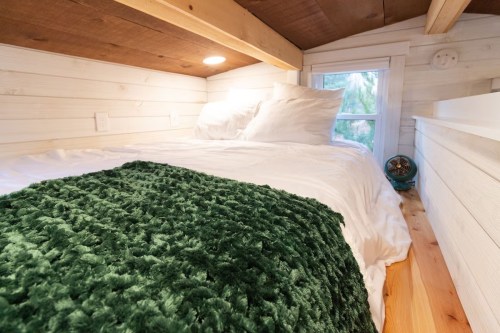 Cozy loft bedroom with white bedding, a green throw blanket, and a window letting in natural light.