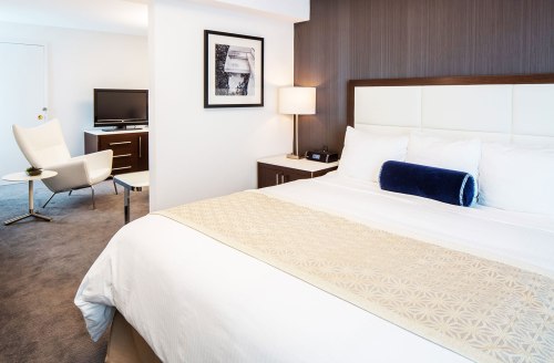 A modern hotel room featuring a bed, a chair, a TV, and stylish decor in neutral tones.