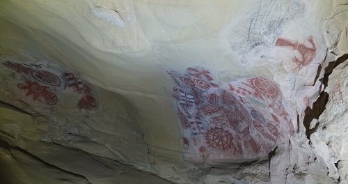 Ancient cave paintings on a rocky ceiling, featuring red and black geometric designs and symbols.