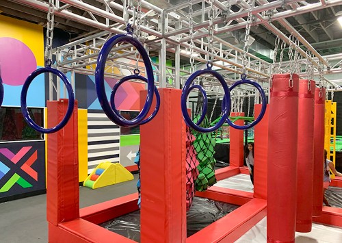 Colorful indoor playground featuring hanging rings, padded obstacles, and vibrant wall designs.