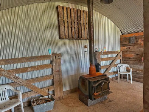 Interior of a rustic cabin with a wood stove, metal walls, wooden accents, and plastic chairs.