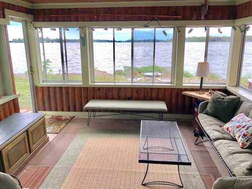 Cozy sunroom with a view of a lake, featuring a bench, coffee table, and comfortable seating.