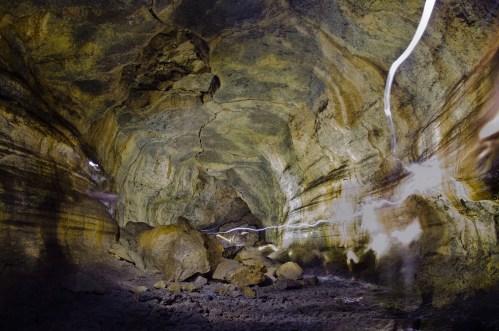 A dimly lit cave interior with textured rock walls and scattered boulders, illuminated by faint light trails.