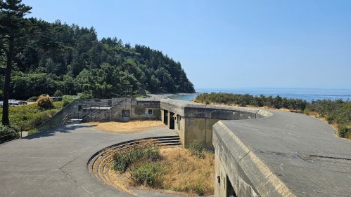 A curved concrete structure overlooks a coastal landscape with trees and a clear blue sky.