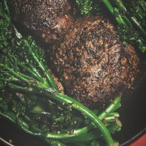 Two cooked patties on a bed of sautéed greens, including broccolini, in a skillet.