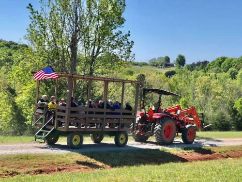 A tractor pulls a wagon filled with people along a scenic, green landscape under a clear blue sky.