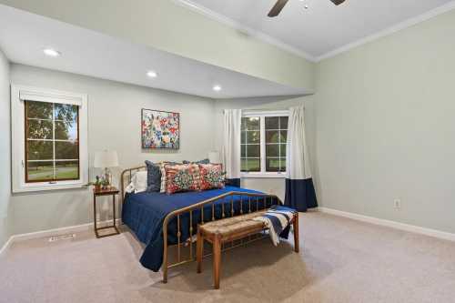 A cozy bedroom featuring a bed with colorful pillows, a wooden bench, and large windows with natural light.