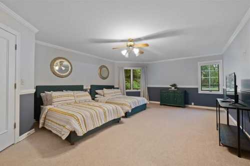 Spacious bedroom with two beds, a TV, and large windows, featuring light blue walls and neutral carpet.