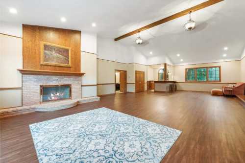 Spacious living room with a fireplace, hardwood floors, and large windows, featuring a decorative area rug.