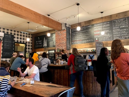 A cozy café interior with patrons enjoying drinks, a chalkboard menu, and a rustic wooden counter.