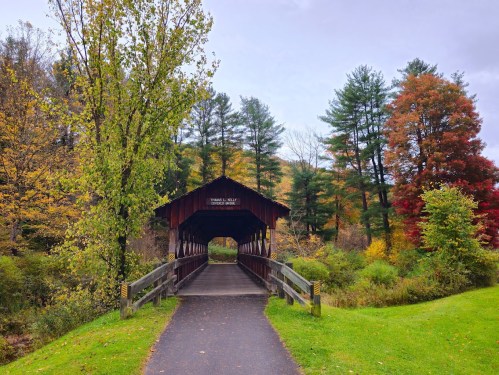 A scenic view of a covered bridge surrounded by colorful autumn trees and a pathway leading through a lush landscape.
