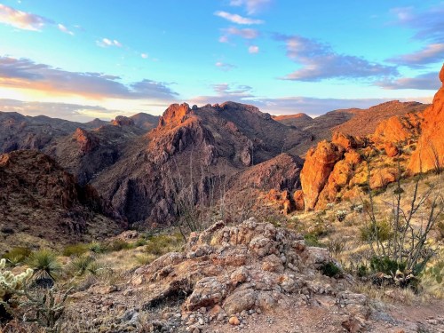 A scenic view of rugged mountains at sunset, with warm colors illuminating the landscape and a clear blue sky.
