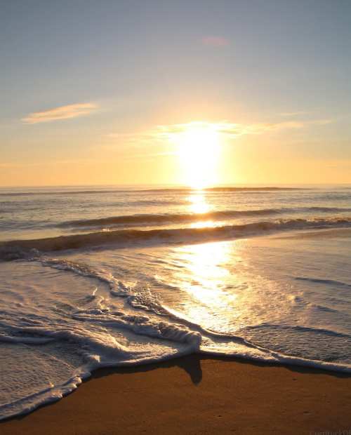 A serene beach scene at sunset, with gentle waves lapping at the shore and a golden sun reflecting on the water.
