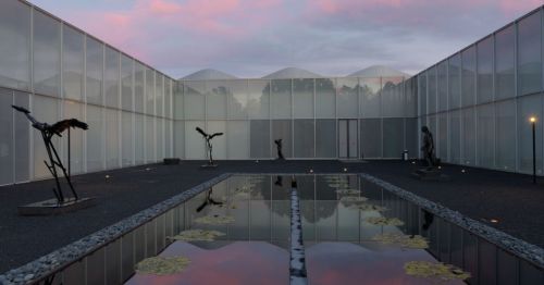 A serene courtyard with sculptures, a reflective pond, and a cloudy sky at dusk.