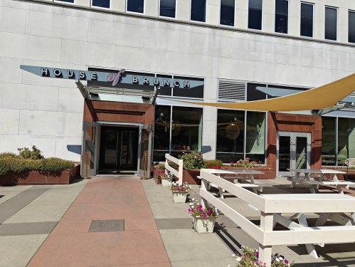 Exterior of "House of Brunch" restaurant with a modern entrance and outdoor seating area, featuring planters and shade sails.