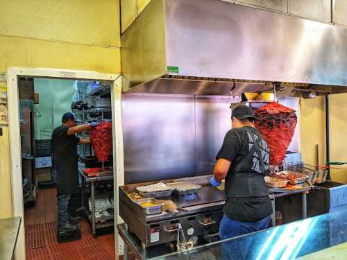 Two cooks in a restaurant kitchen preparing food, with a large vertical grill in the background.