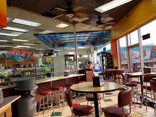 Interior of a casual diner with colorful walls, round tables, and red stools, featuring a counter and vending machines.