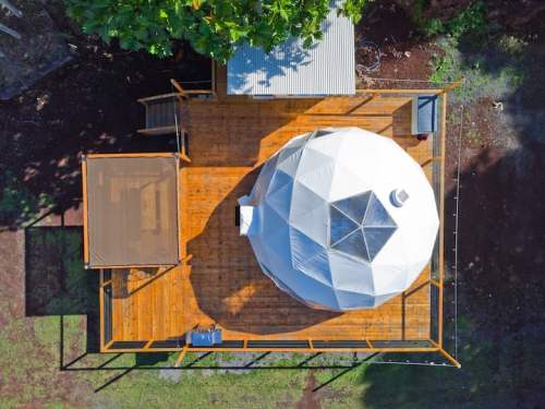 Aerial view of a geodesic dome on a wooden deck surrounded by greenery.