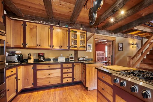 A rustic kitchen with wooden cabinets, a gas stove, and exposed beams, featuring warm tones and a cozy atmosphere.