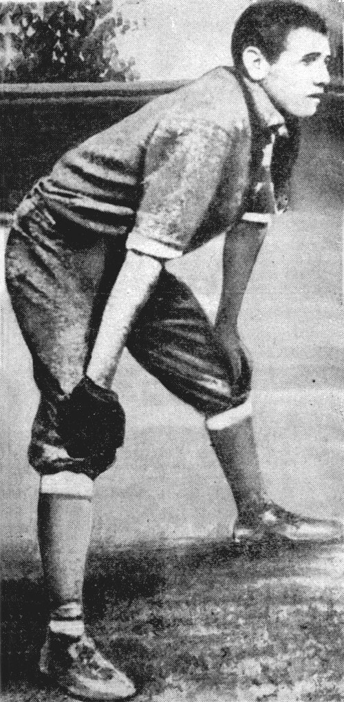 A vintage black-and-white photo of a young male baseball player in a crouched stance, wearing a uniform and glove.
